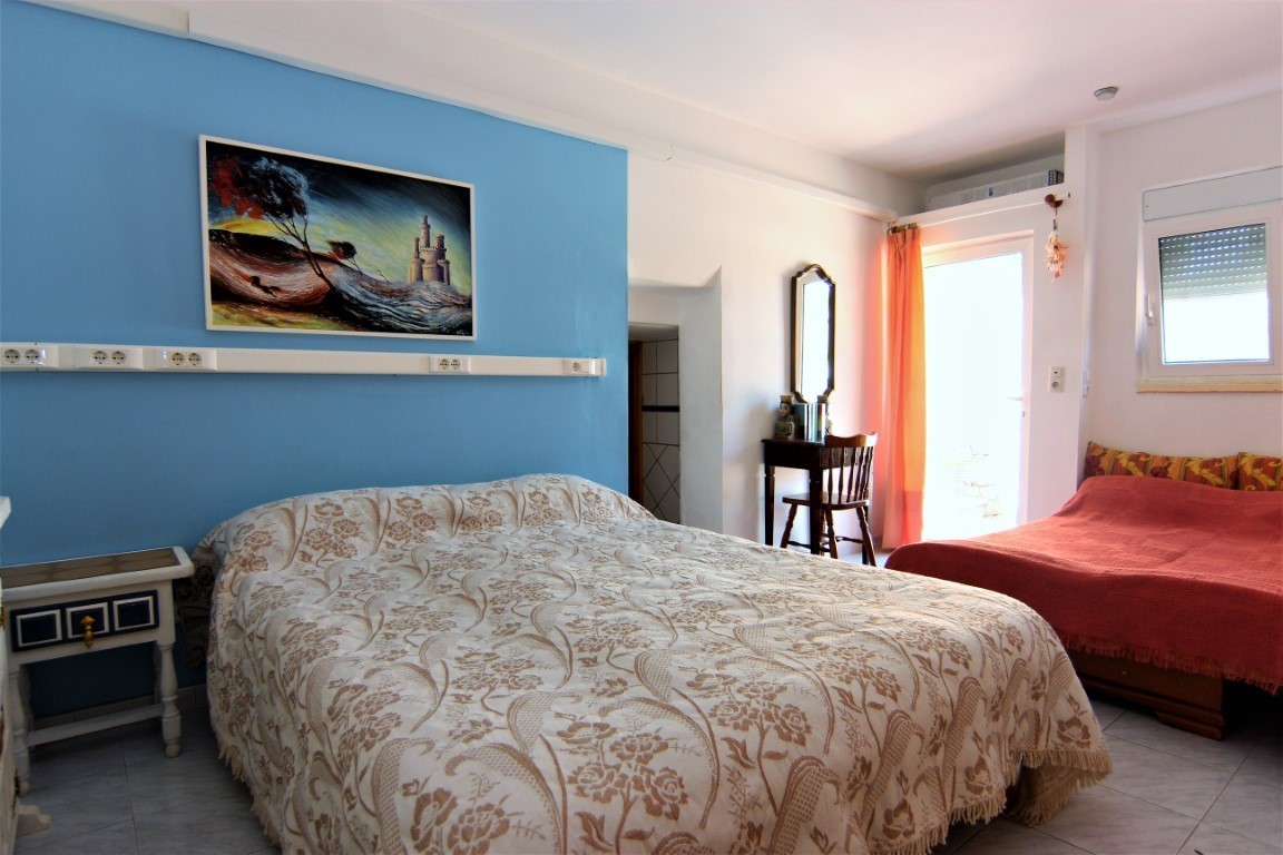 Lichte slaapkamer met een blauwe accentmuur, een tweepersoonsbed met bloemmotief en een extra eenpersoonsbed. Voorzien van een houten bureau en directe toegang tot buiten.