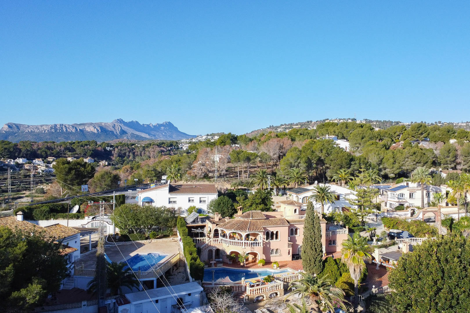 Luchtfoto van de mediterrane villa met niervormig zwembad, boogvormige terrassen en volgroeide tuinen met uitzicht op de bergen.