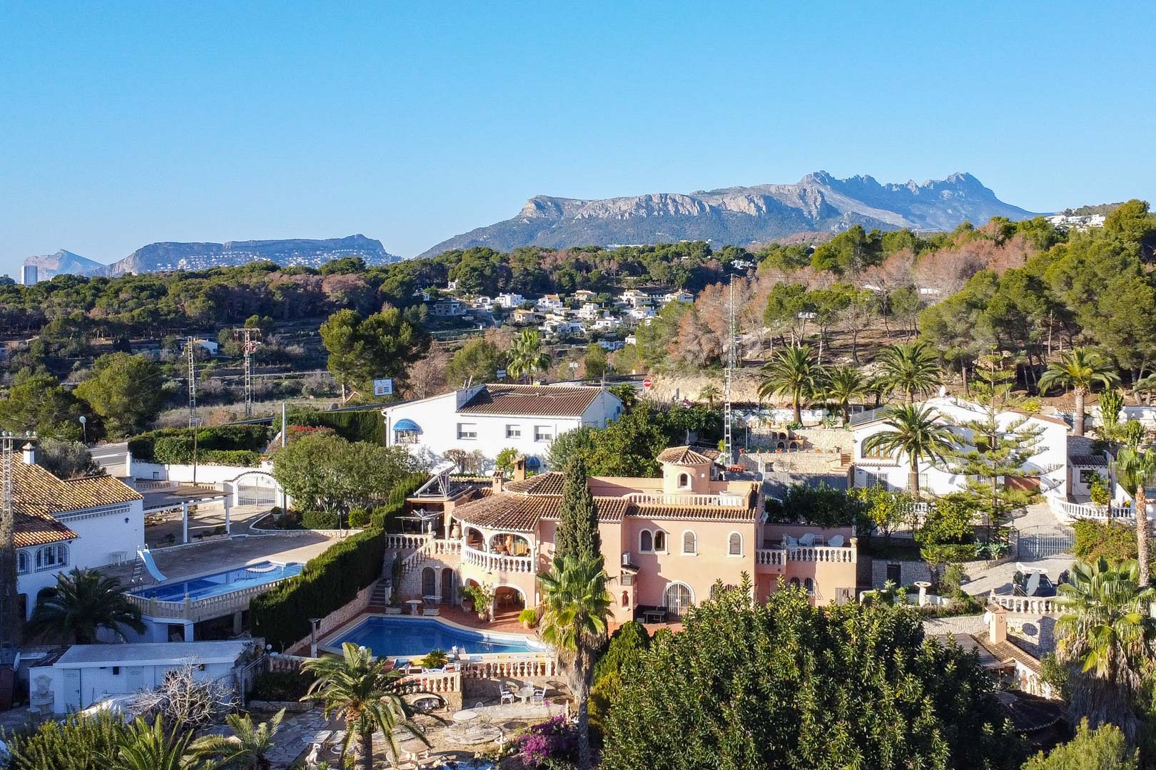 Luchtfoto van de mediterrane villa met privézwembad en ruime terrassen, gelegen in een groene omgeving met uitzicht op de nabijgelegen bergen.