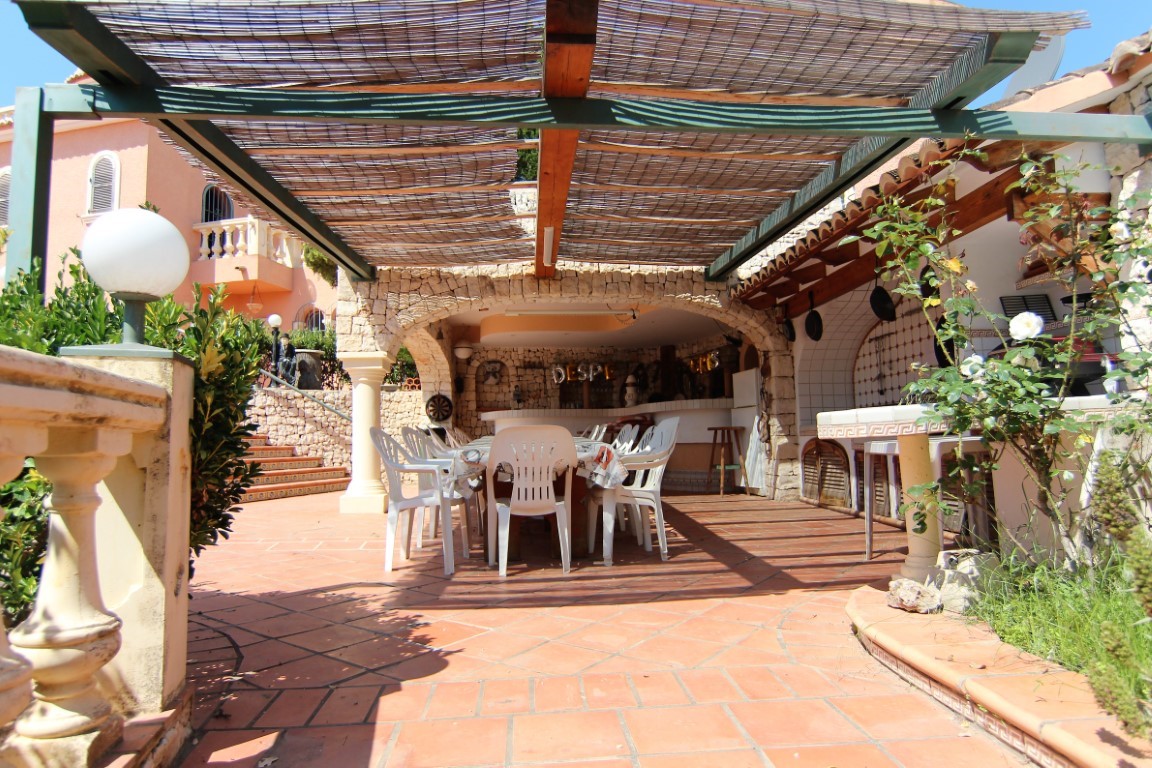 Overdekt buitenterras met rieten pergola, grote eethoek en buitenkeuken onder rustieke stenen bogen en een vloer van authentieke terracotta tegels.