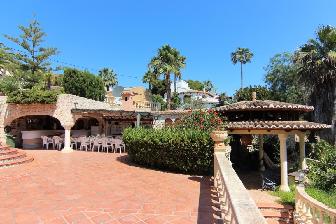 Royaal terras met terracotta tegels, een overdekte eethoek onder stenen bogen en een apart paviljoen omgeven door palmbomen en mediterrane tuinen.