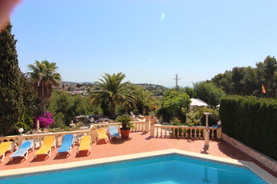 Ruim terras bij het zwembad met terracotta tegels, ligstoelen en een klassieke balustrade met uitzicht op de mediterrane tuinen en de kustlijn.