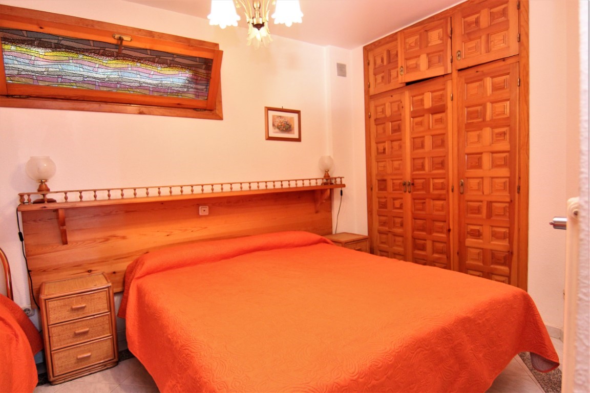 Slaapkamer met een ingebouwde houten kledingkast, een hoofdbord met geïntegreerde plank en een decoratief glas-in-loodraam boven het bed.
