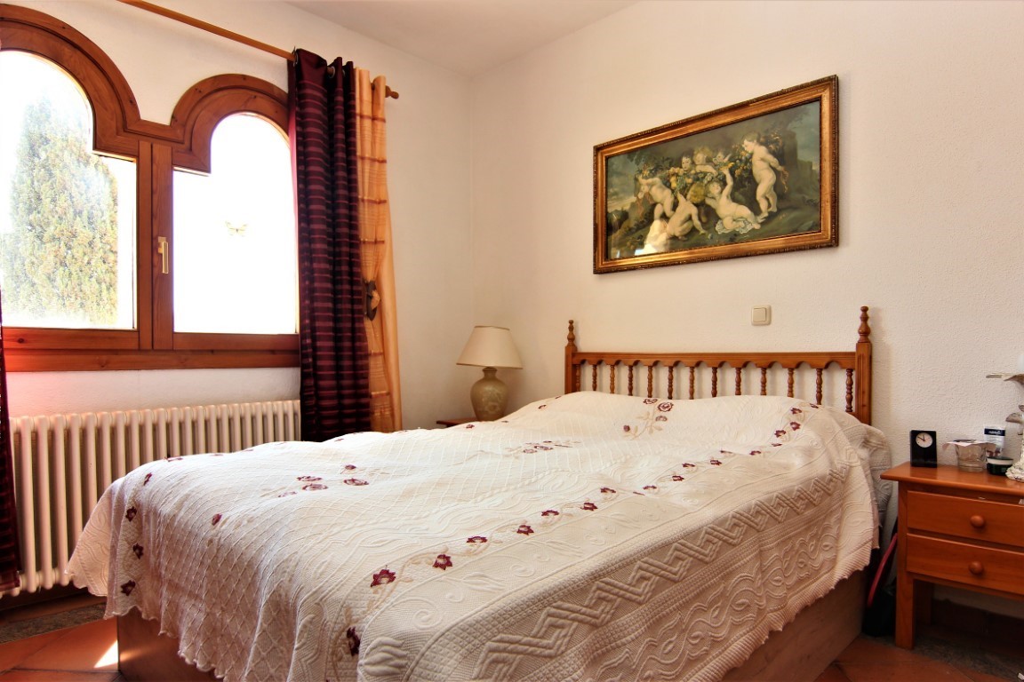 Slaapkamer met tweepersoonsbed, houten hoofdbord en traditionele boogramen. Voorzien van een terracotta vloer, klassieke radiator en natuurlijke lichtinval.