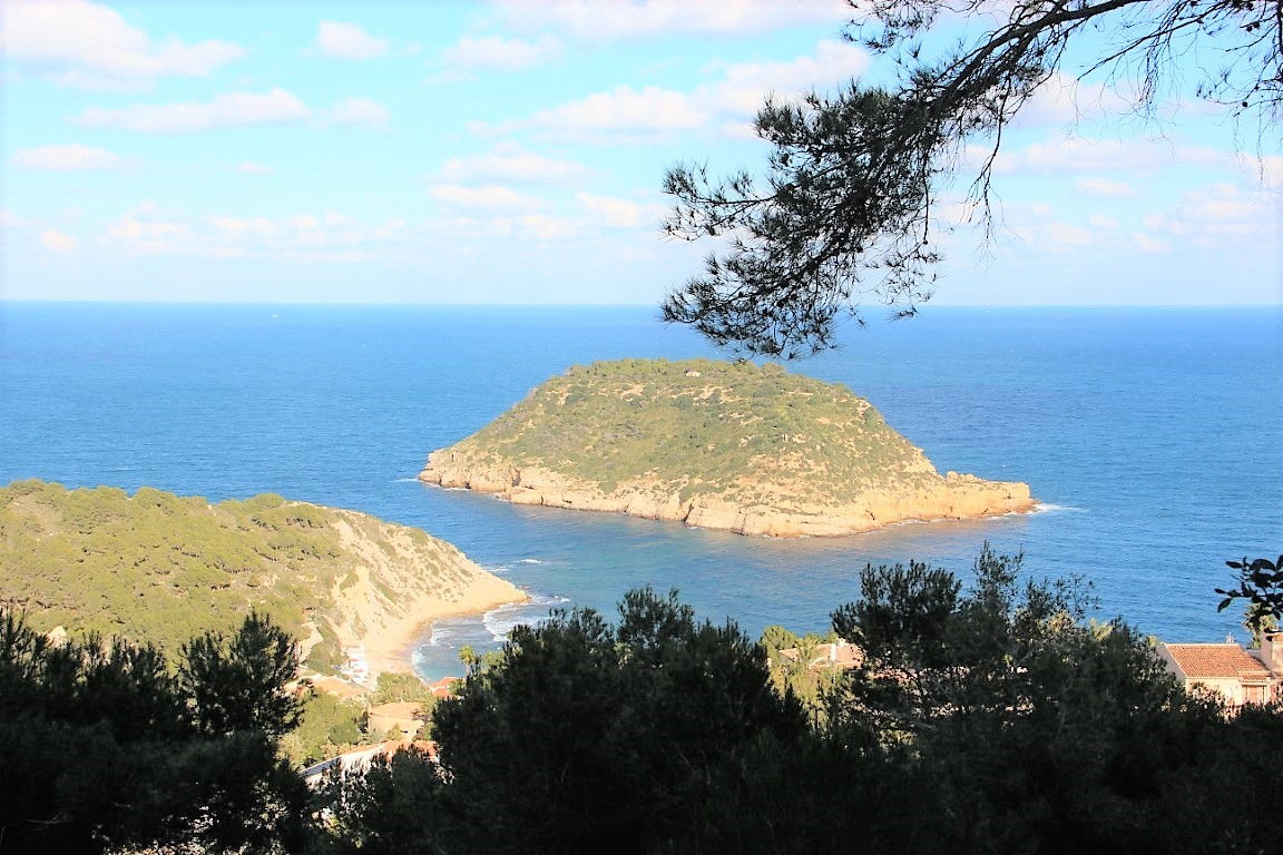 Panoramisch uitzicht vanaf het perceel op het eiland Portichol en de Middellandse Zee, omlijst door pijnbomen en de kustlijn van Jávea.
