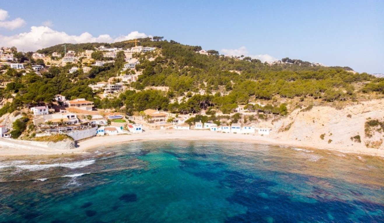 Luchtfoto van de baai van Portichol met traditionele witte huisjes, turquoise water en de rotsachtige kustlijn van Jávea.