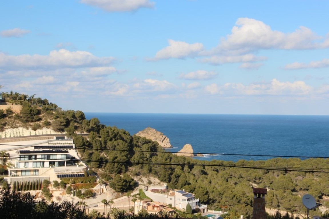 Panoramisch uitzicht op de Middellandse Zee en de kust van Jávea, met dennenbossen op de heuvels en moderne villa's die opgaan in het natuurlijke landschap.