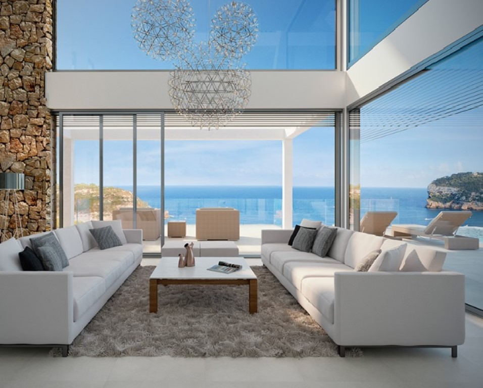 Woonkamer met dubbele hoogte, kamerhoge glazen puien, een natuurstenen wand en designverlichting met panoramisch uitzicht op de Middellandse Zee.