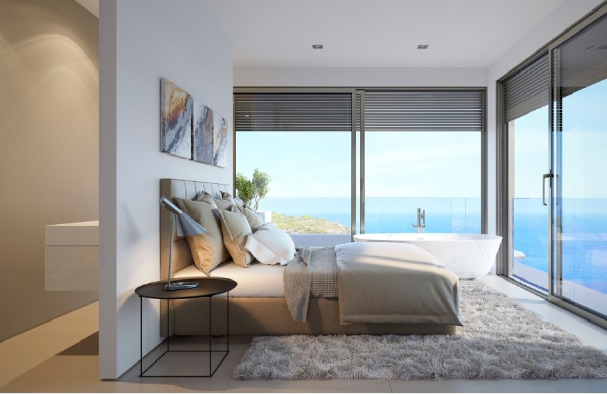 Hoofdslaapkamer met vrijstaand bad bij kamerhoge ramen, met panoramisch uitzicht op zee en een strak, modern interieur.