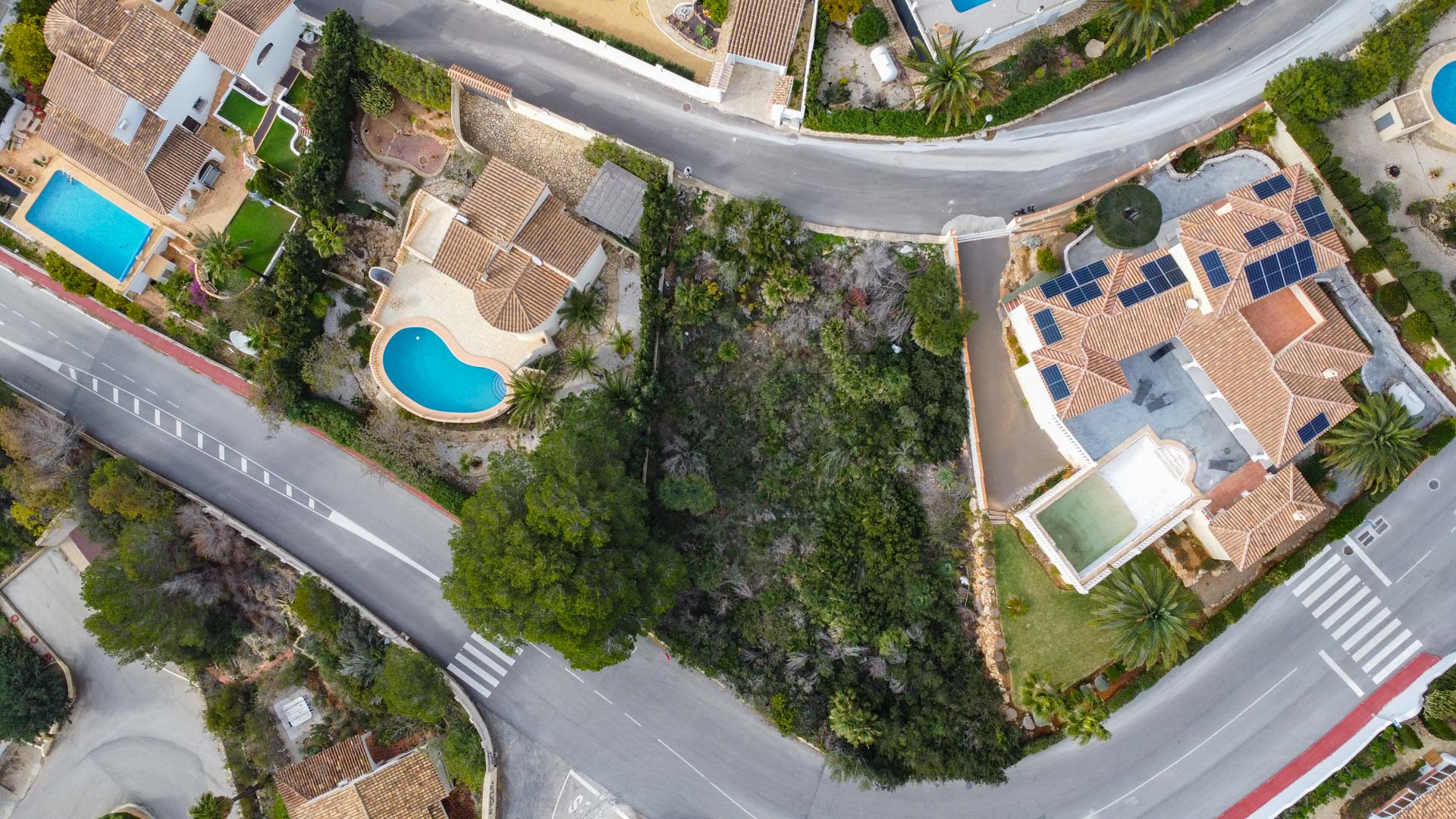 Bovenaanzicht van de woonwijk met mediterrane pannendaken, privézwembaden, zonnepanelen en de omliggende infrastructuur en vegetatie.