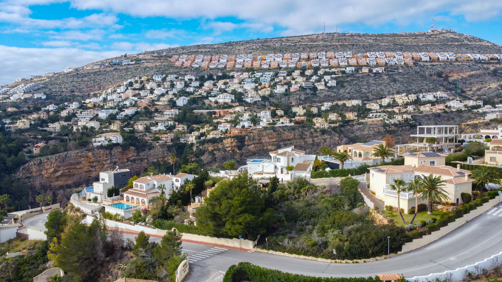 Panoramisch luchtfoto van de woonwijk in Cumbre del Sol, met villa's op de heuvelrug omgeven door mediterrane begroeiing en kronkelende wegen.