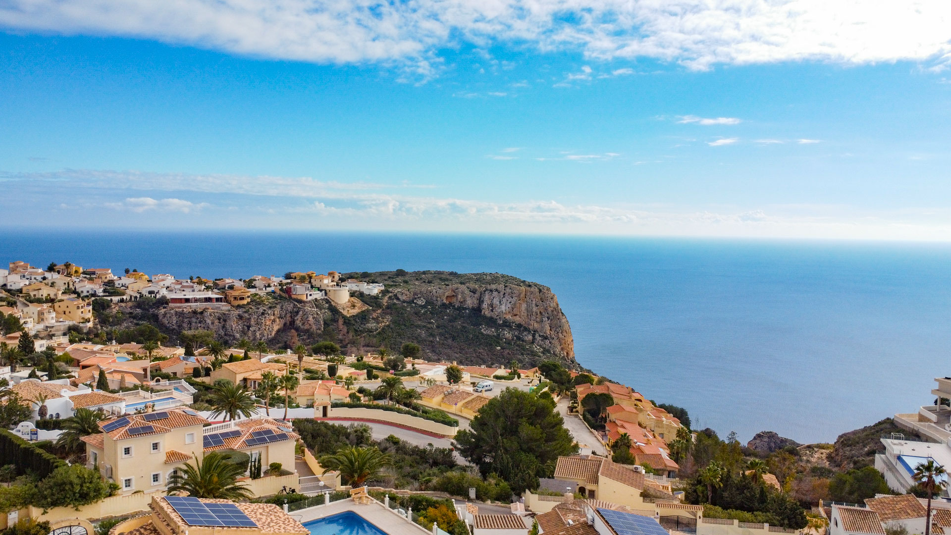 Verhoogd panoramisch uitzicht over Cumbre del Sol met mediterrane villa's, zonnepanelen, kustkliffen en de uitgestrekte blauwe horizon van de Middellandse Zee.