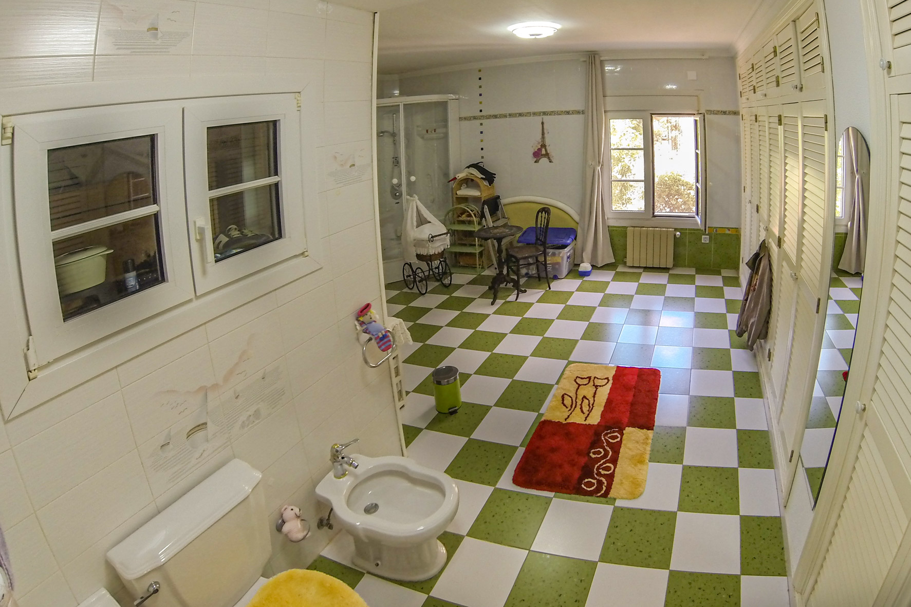 Badkamer met groen-wit betegelde vloer, wit toilet en bidet, en een raam dat zorgt voor natuurlijk licht.