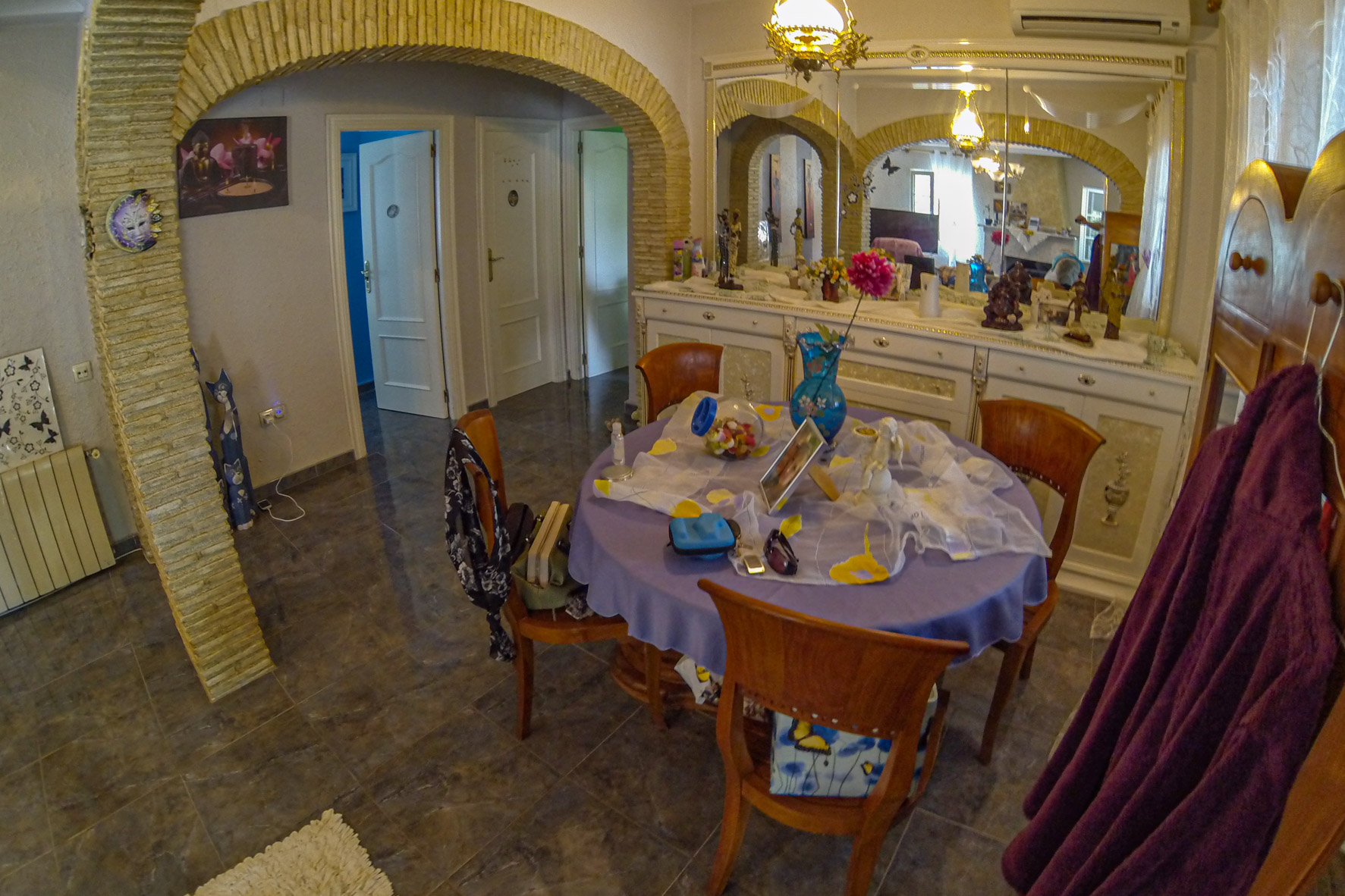 Eetkamer met stenen bogen, een ronde tafel met een lila tafelkleed en een sierlijk wit dressoir met spiegel.