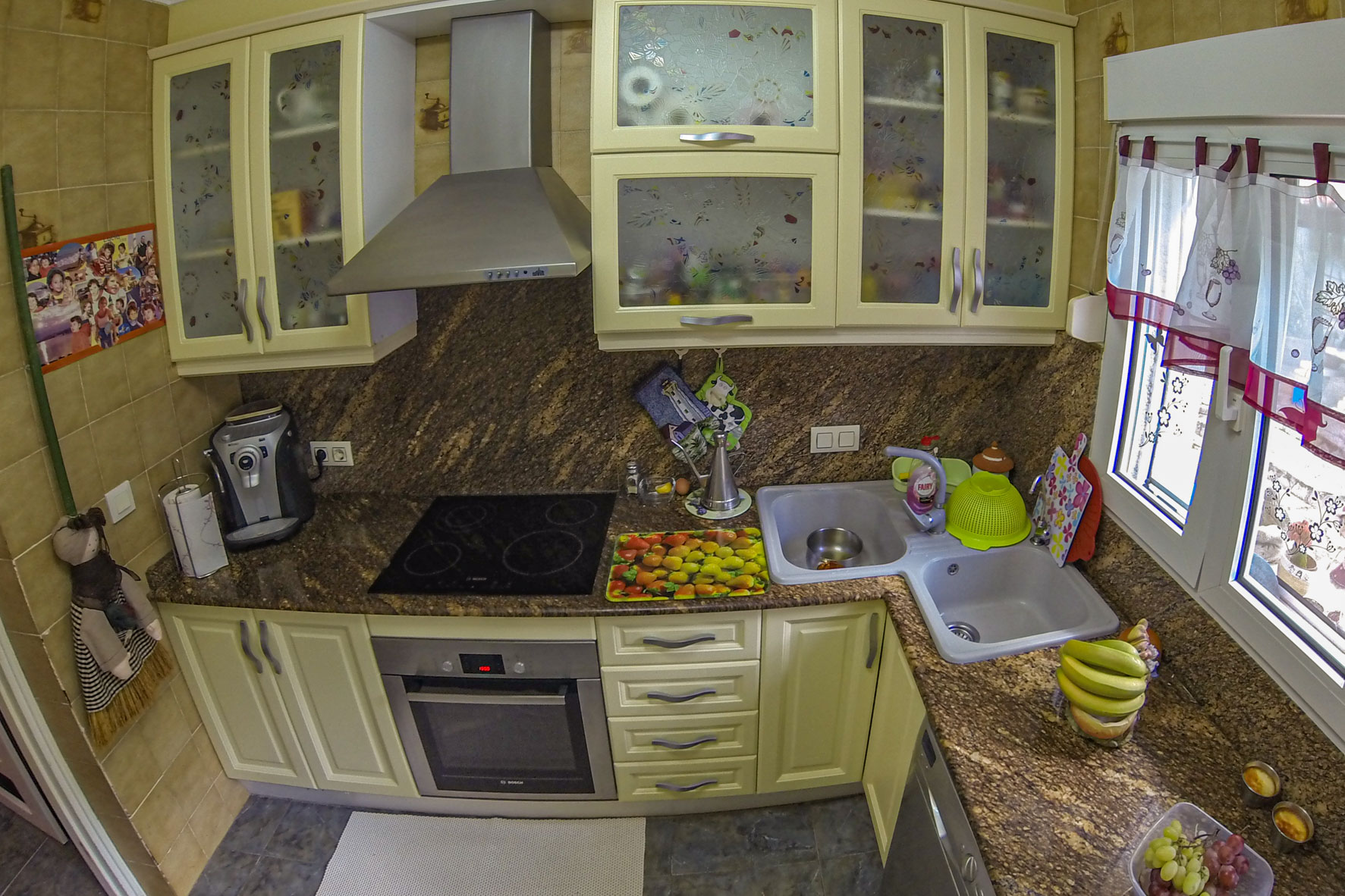 Keuken met bruin granieten aanrechtblad, moderne apparatuur en crèmekleurige kasten.