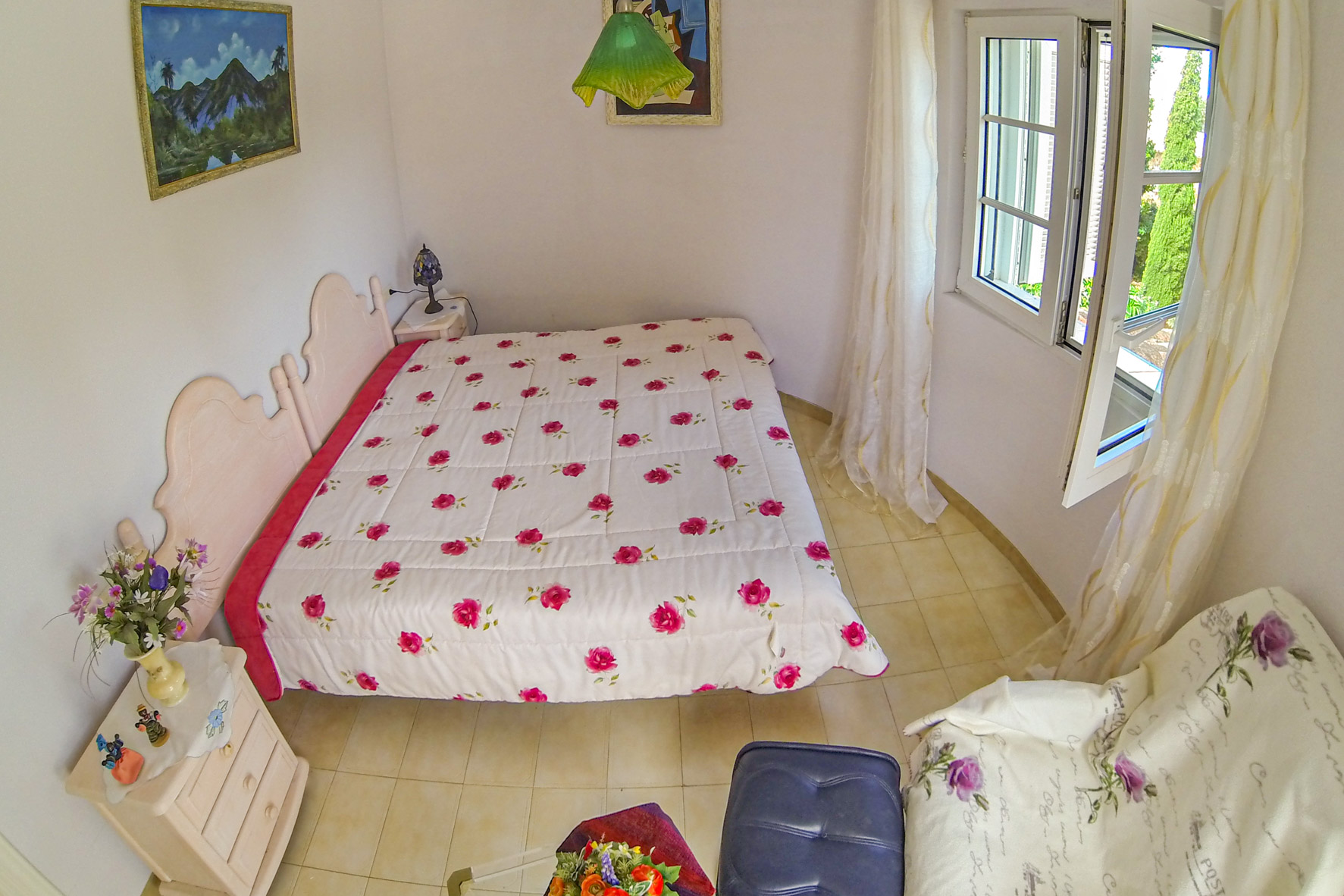 Lichte slaapkamer met een tweepersoonsbed, bloemmotief beddengoed en een raam met transparante gordijnen.