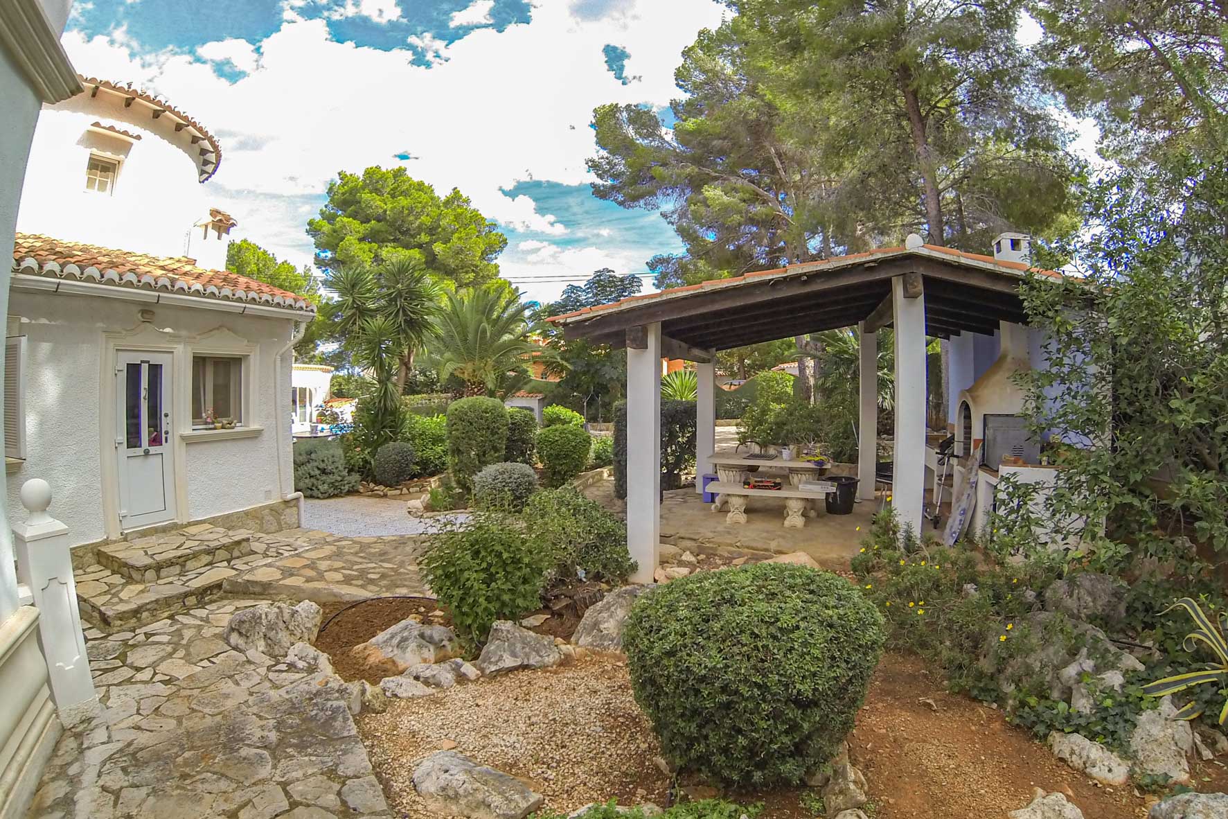 Overdekte barbecueplaats met houtoven en stenen tafel in een mediterrane tuin.