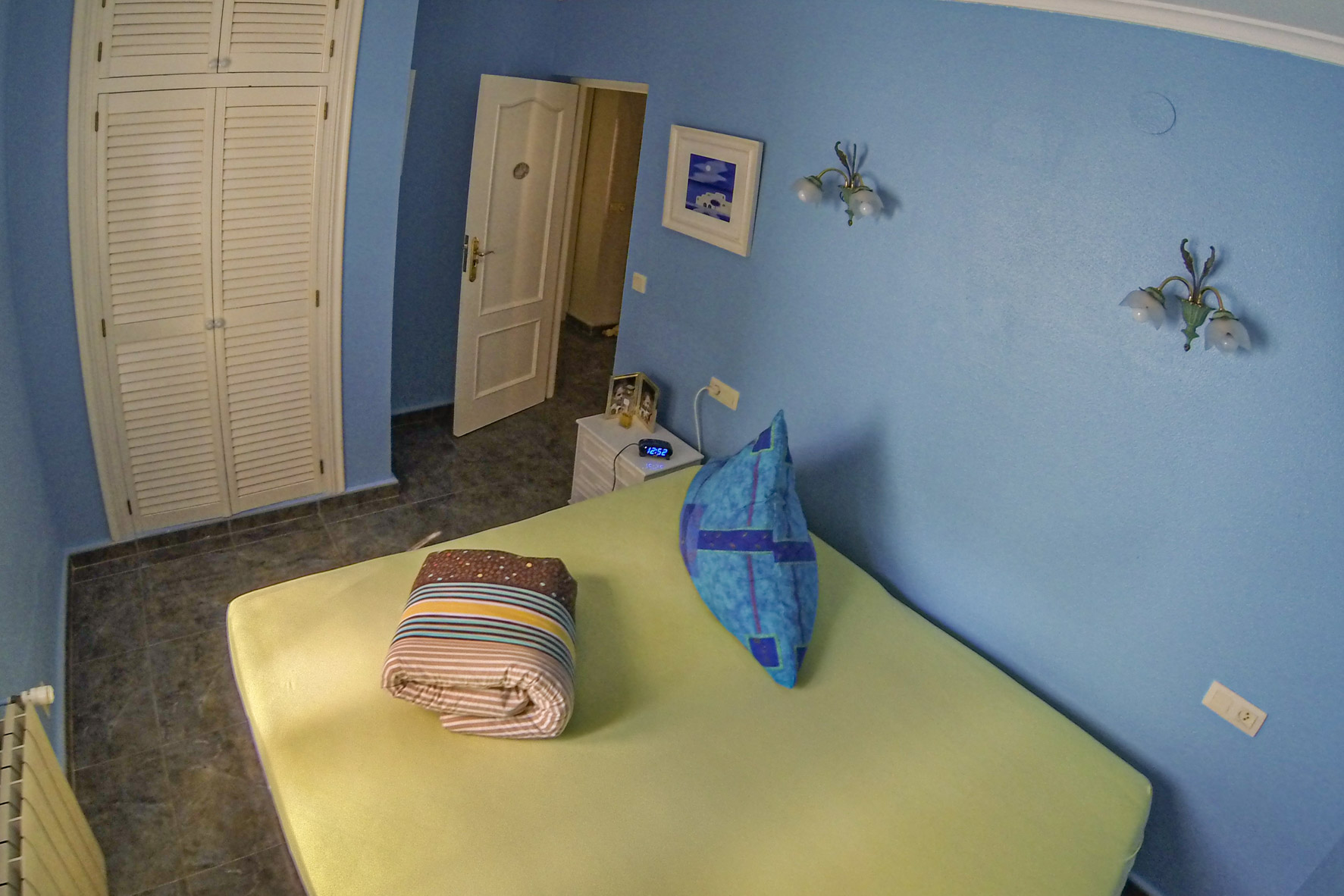 Slaapkamer met blauwe muren, een ingebouwde witte houten kast en opgevouwen beddengoed.