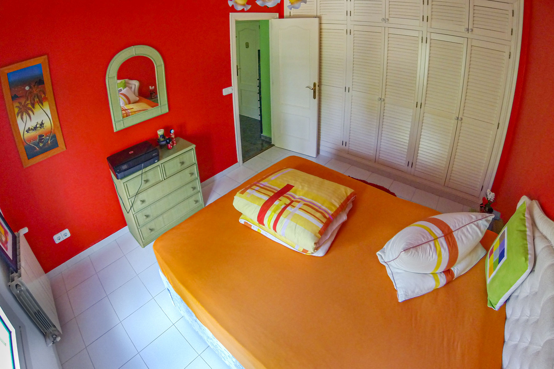 Slaapkamer met rode muren, witte inbouwkast en een bed met oranje beddengoed.