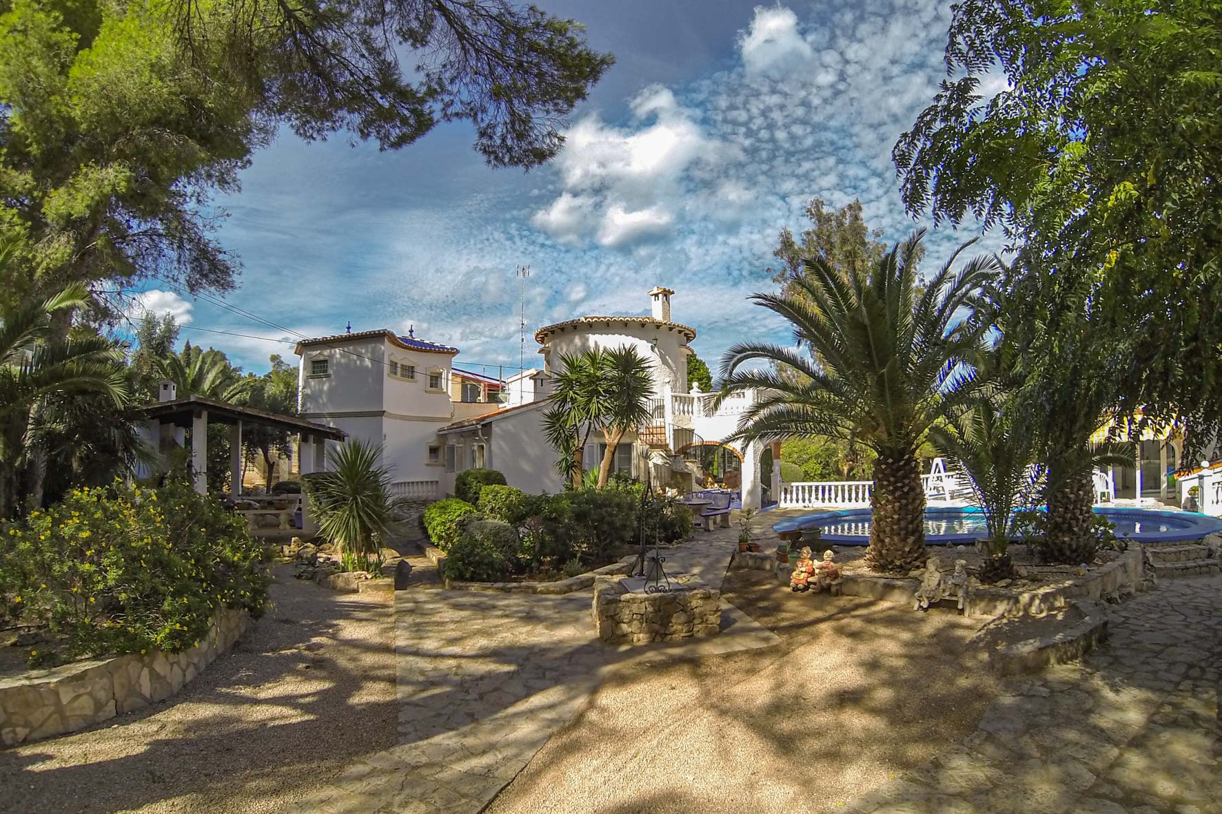 Uitzicht op de volgroeide tuin met een cirkelvormig zwembad en het hoofdgebouw in mediterrane stijl.