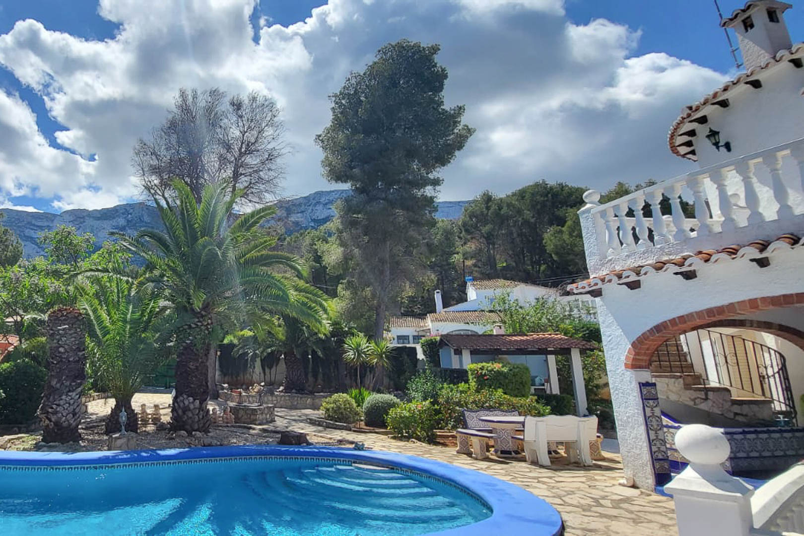 Uitzicht op het blauwe zwembad met getrapte toegang, omgeven door tuinen en het hoofdhuis in Denia.