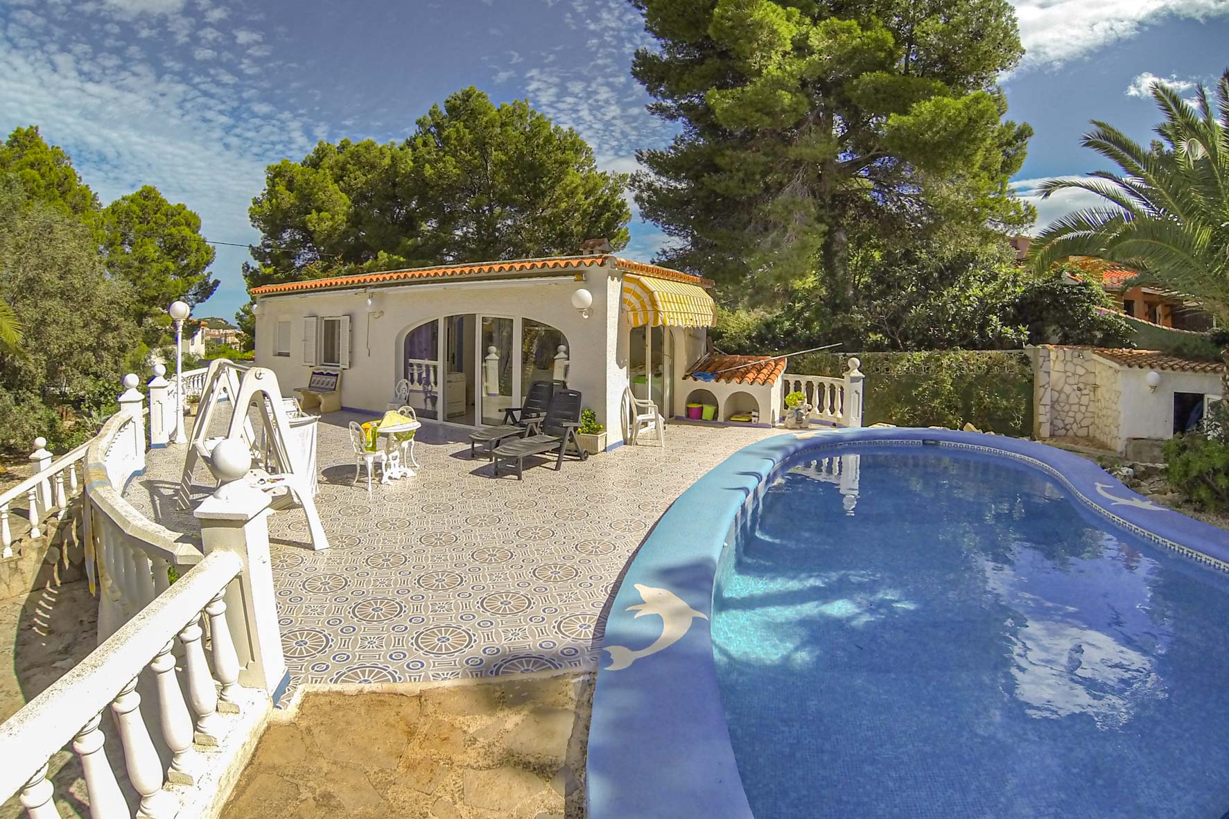 Uitzicht op het privézwembad met blauwe mozaïektegels en het poolhouse met gele luifel.