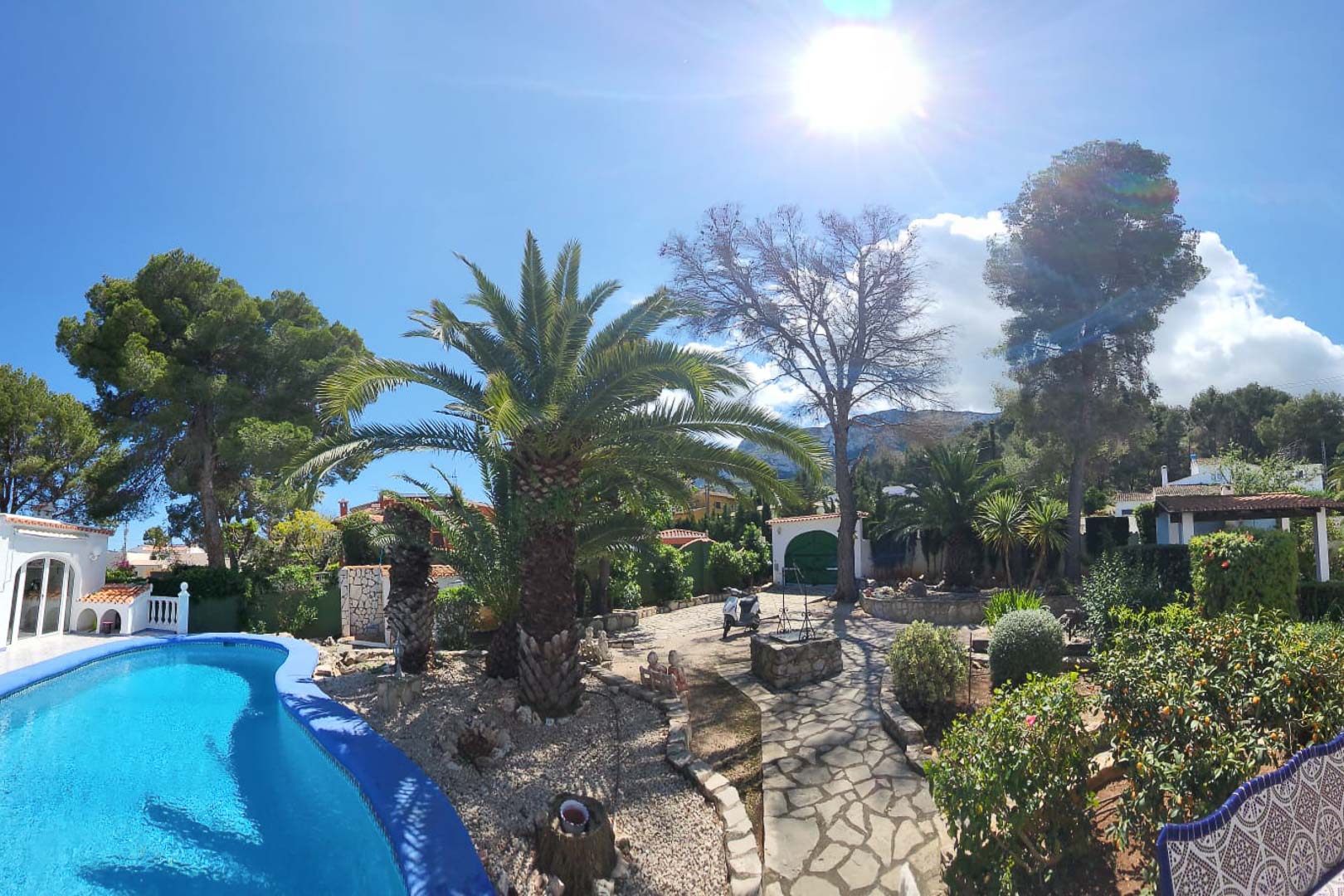 Uitzicht op het turquoise blauwe zwembad en de tuinen met palmbomen en stenen pad in Denia.