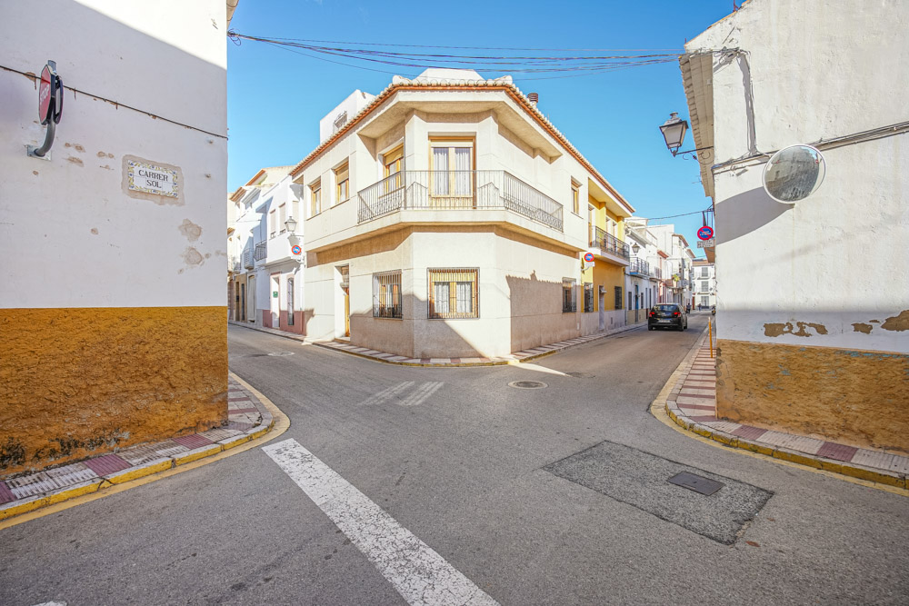 Buitenaanzicht van een traditioneel hoekhuis in Gata de Gorgos, voorzien van een balkon met smeedijzeren hekwerk en klassieke raamroosters in een rustige straat.