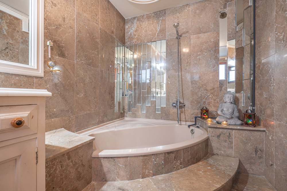 Elegante badkamer met een ingebouwd hoekbad, wanden van gepolijst marmer en een unieke verticale spiegelwand.