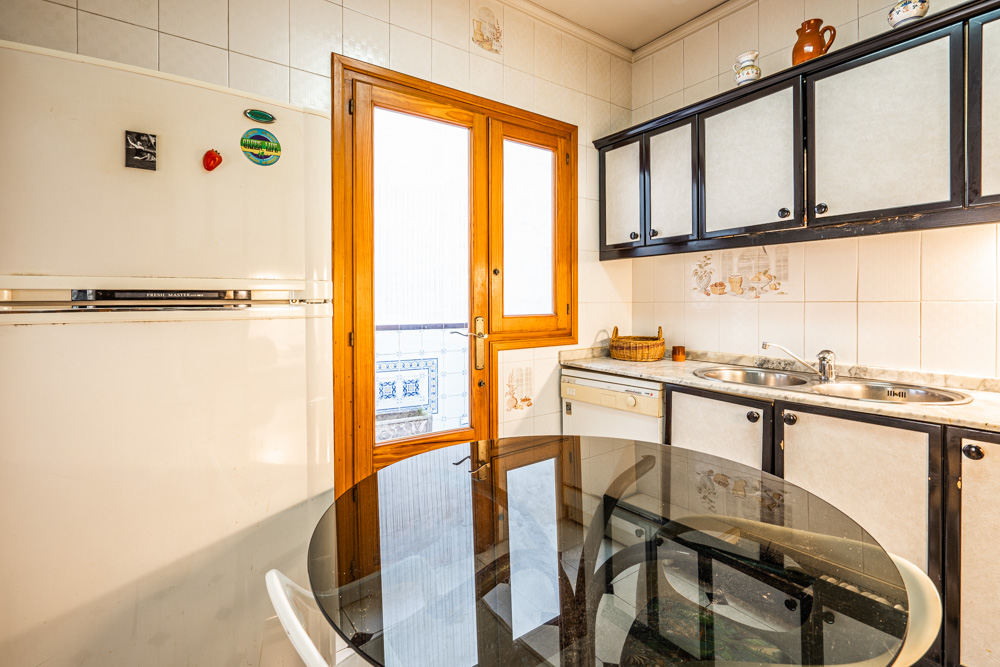 Functionele keuken met donker afgewerkte kasten, marmeren aanrechtblad en een houten glasdeur die toegang biedt tot de patio. Voorzien van een glazen eettafel.