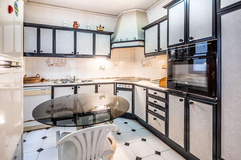 Functionele keuken met wit-donkere kasten, inbouwapparatuur, een marmeren werkblad en een glazen eettafel op een karakteristieke zwart-witte tegelvloer.