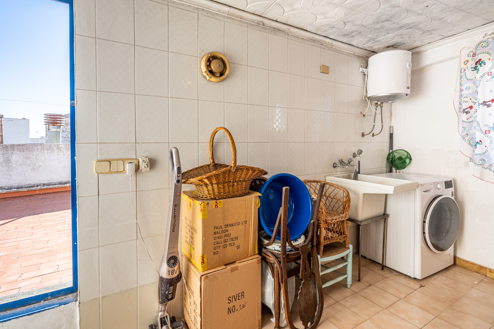 Praktische wasruimte en berging voorzien van een wasmachine, elektrische boiler en directe toegang tot het dakterras met terracotta tegels.