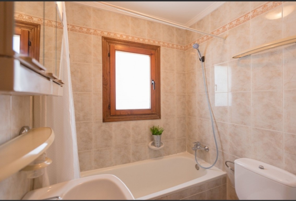 Functionele badkamer met ligbad, beige wandtegels met decoratieve rand en een houten raam dat zorgt voor natuurlijk lichtinval.