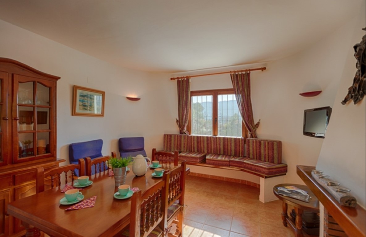 Traditionele eethoek met houten tafel, klassieke vitrinekast en een ingebouwde bank onder het raam met uitzicht op het landschap.