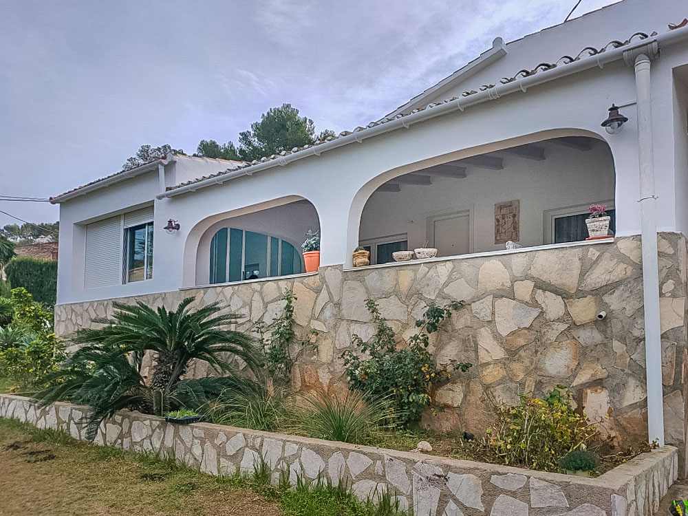 Exterieur van de villa met een traditionele naya met bogen en een gevel van natuursteen. De tuin is voorzien van mediterrane beplanting en een stenen muur.