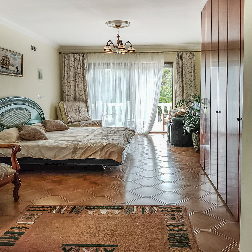 Lichte slaapkamer met kamerhoge houten inbouwkasten, een betegelde vloer met ruitpatroon en directe toegang tot het terras via grote schuifdeuren.