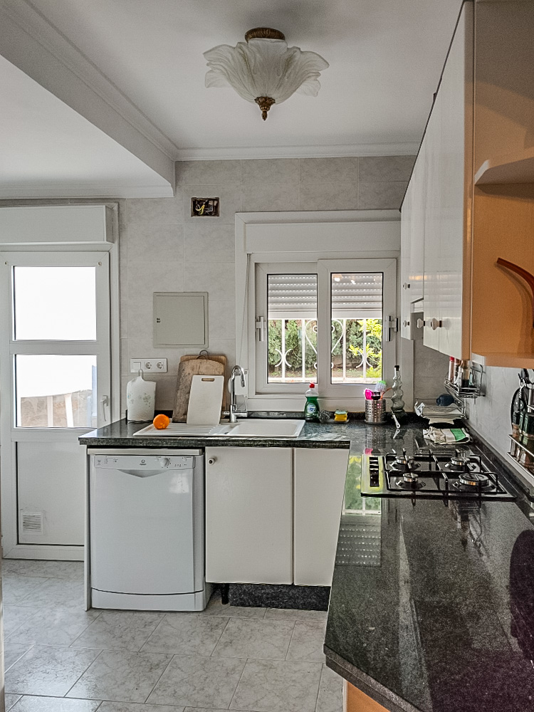 Praktische keuken met een donker granieten aanrechtblad, gaskookplaat en witte kasten. Voorzien van een vaatwasser en directe toegang tot de buitenruimte.