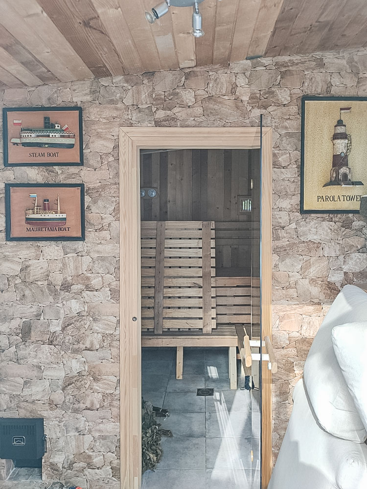Privésauna met natuurstenen muren en een glazen deur. Het interieur is volledig afgewerkt met hout en voorzien van zitbanken op meerdere niveaus.