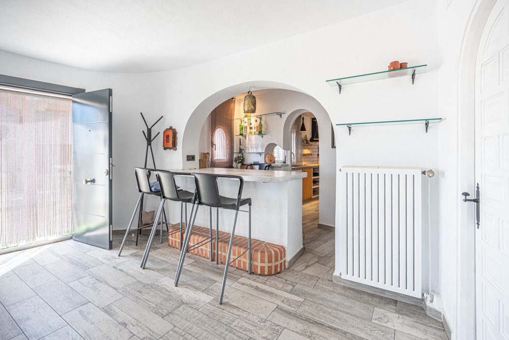 Entree met ontbijtbar voorzien van bakstenen accenten, houtlook vloertegels en een karakteristieke boogdoorgang naar de keuken.