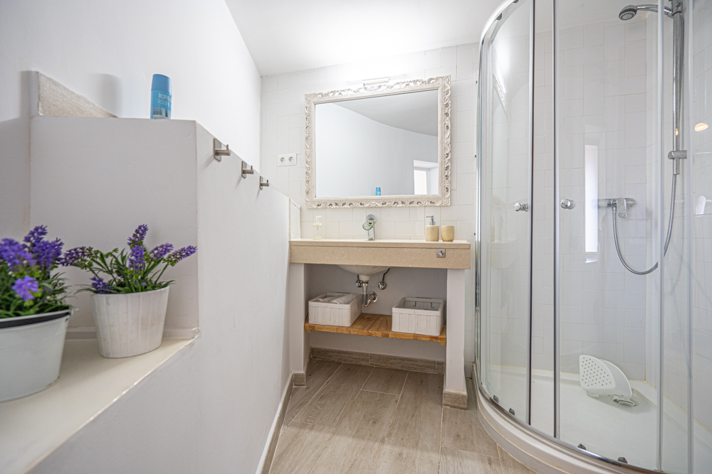 Gerenoveerde badkamer met een halfronde douchecabine, stenen wastafelblad, sierlijke spiegel en keramische vloer met houtlook.