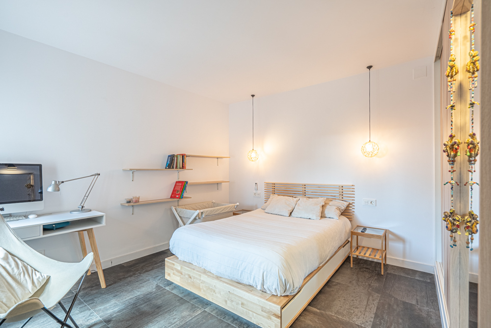 Moderne slaapkamer met houten bed, geïntegreerde werkplek en zwevende planken. Voorzien van design hanglampen en een donkere tegelvloer.