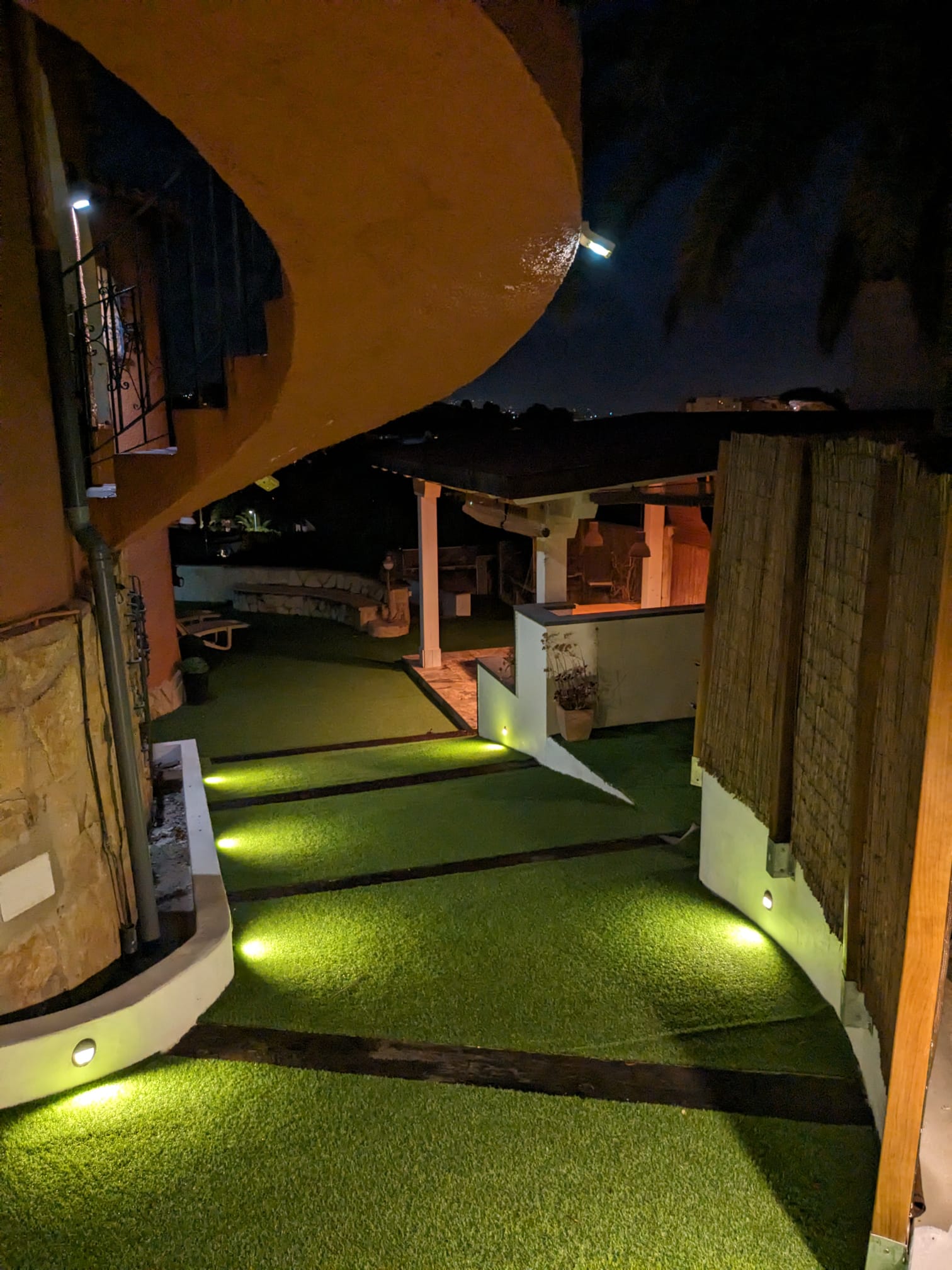 Nachtzicht op de buitenpaden met geïntegreerde LED-vloerverlichting, kunstgras en een overdekte pergola op de achtergrond.