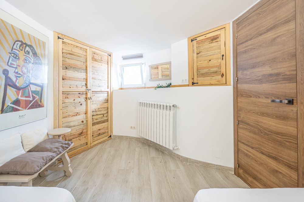 Slaapkamer met ingebouwde kasten van rustiek hout, houtlook tegelvloer, wandradiator en witte muren met artistieke wanddecoratie.