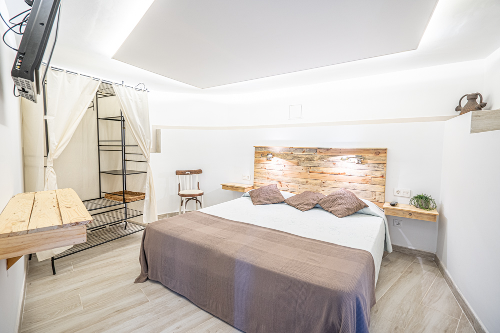 Slaapkamer met rustiek houten hoofdbord, zwevende nachtkastjes, indirecte plafondverlichting en een minimalistische open kledingkast met gordijnen.