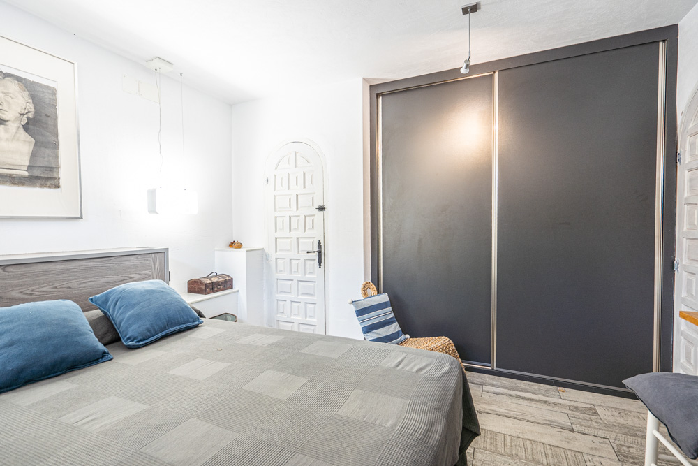 Slaapkamer voorzien van een grote inbouwkast met donkere schuifdeuren, keramische parketvloer en een traditionele witte boogdeur.