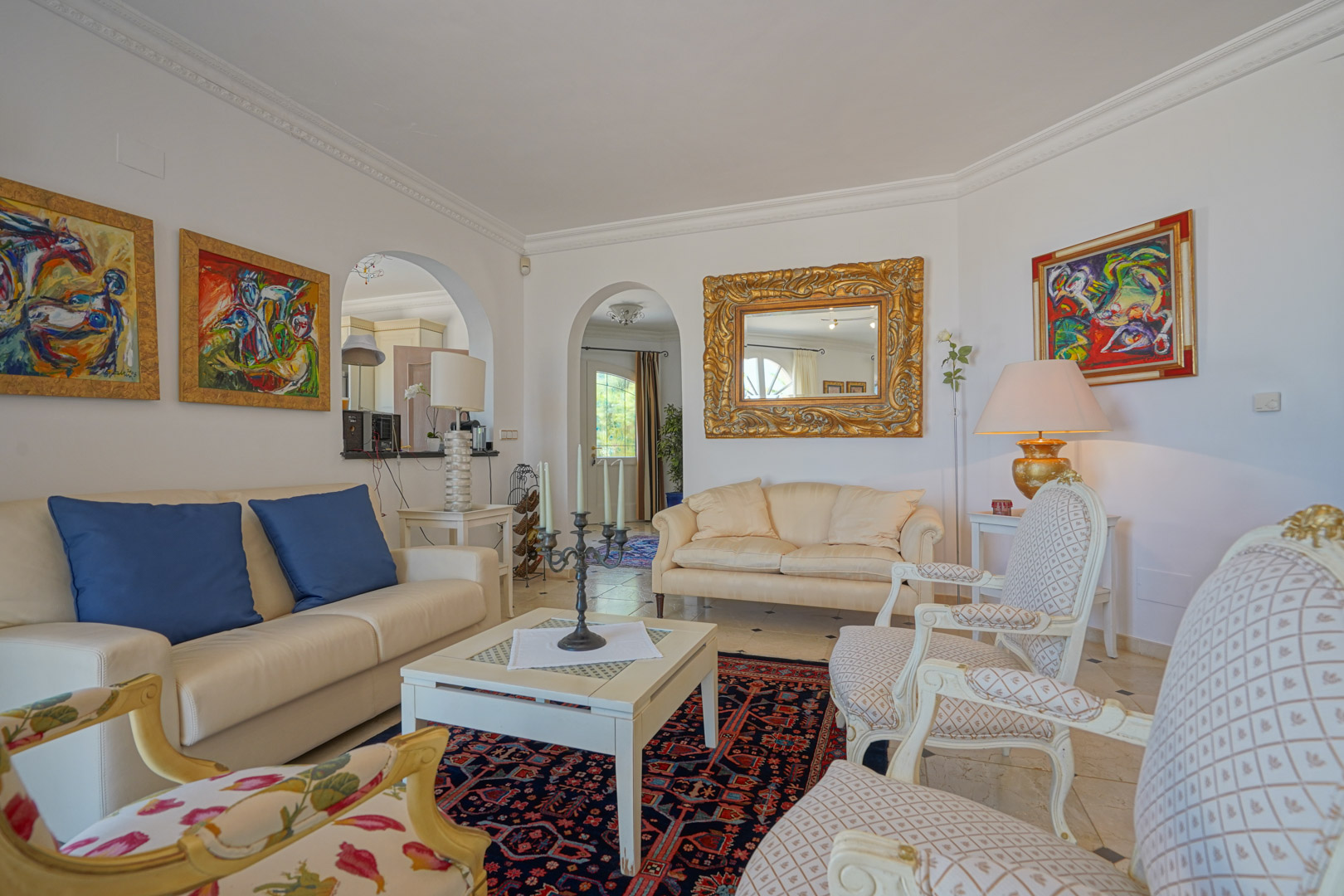 Elegante woonkamer met klassieke fauteuils, lederen banken en architecturale bogen. De ruimte is verfraaid met goudomlijste spiegels, kleurrijke kunst en sierlijsten.