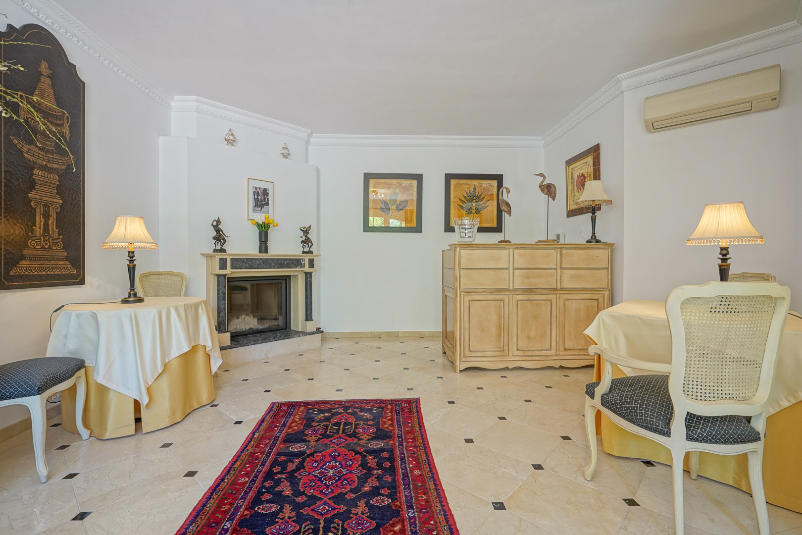 Elegante woonkamer met marmeren open haard, keramische tegelvloer met zwarte accenten en klassiek meubilair onder decoratieve plafondlijsten.
