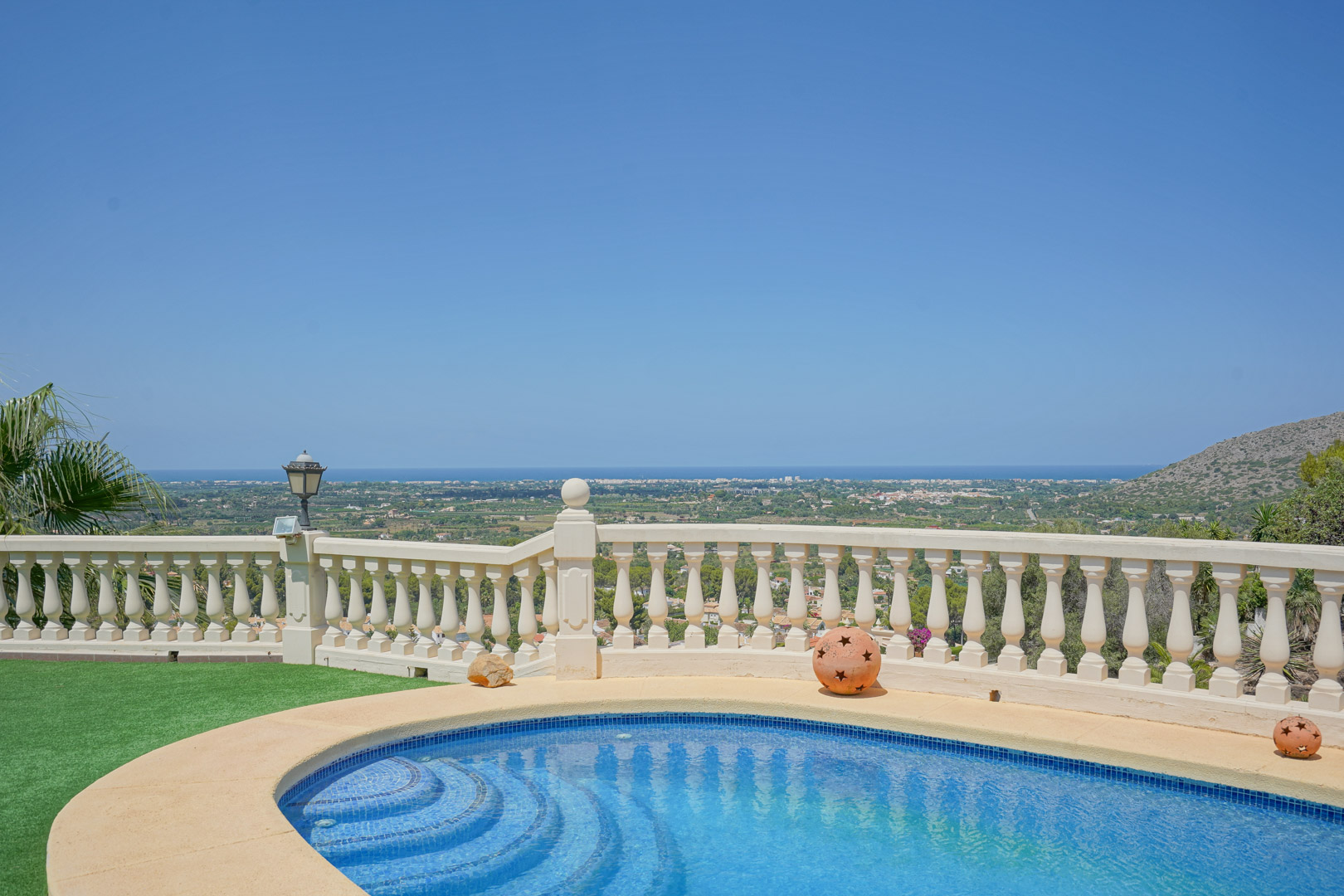Gebogen zwembad met blauwe mozaïektegels en een klassieke balustrade, met een weids panoramisch uitzicht over de vallei en de Middellandse Zeekust.