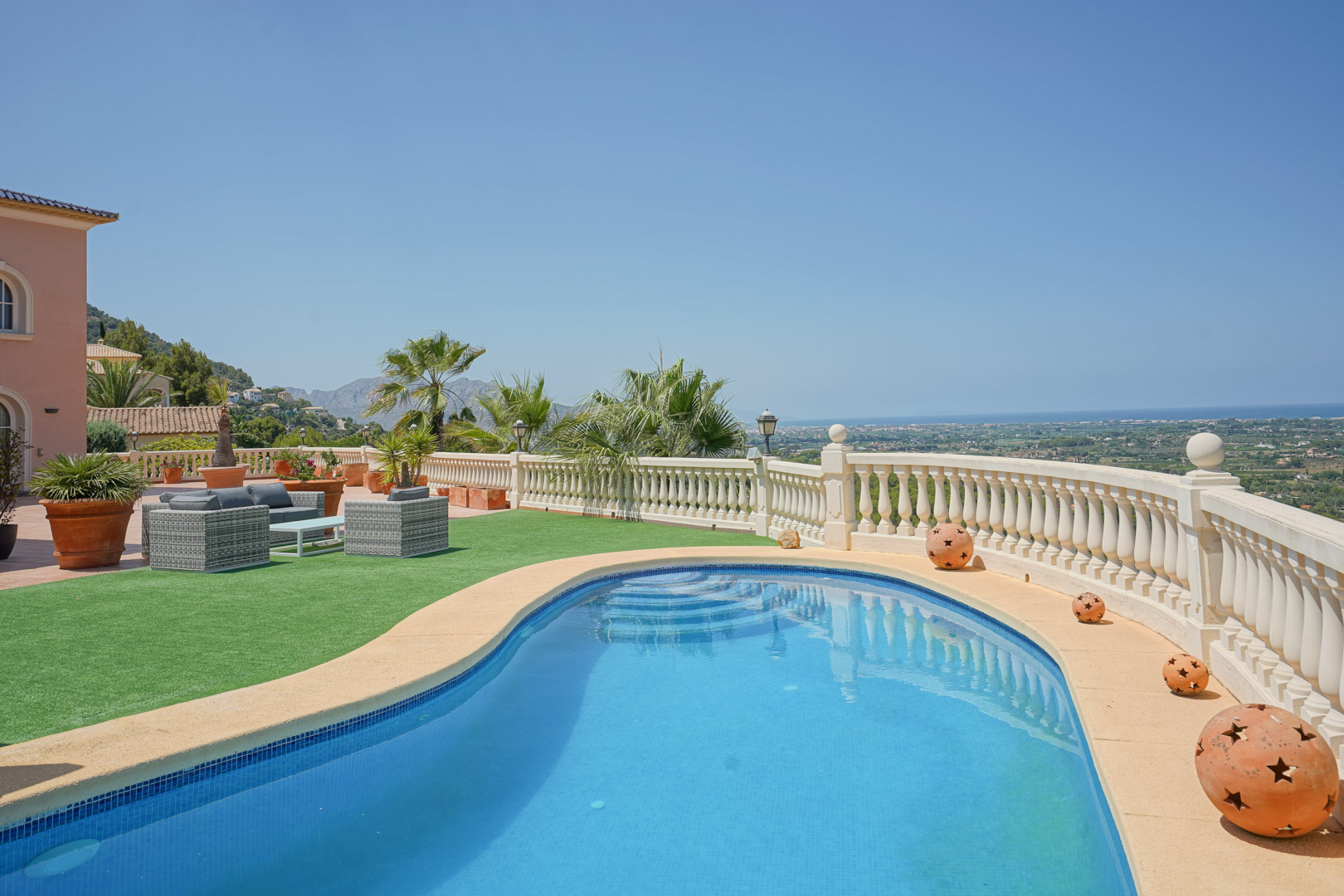 Nier-vormig zwembad met panoramisch uitzicht op zee en de vallei, omzoomd door een klassieke balustrade, kunstgras en een comfortabele loungeset van wicker.