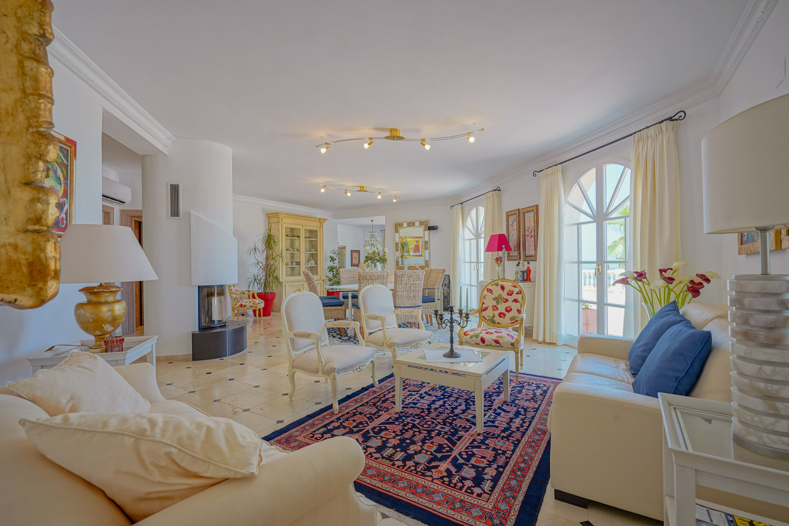 Open woon- en eetkamer met een moderne ronde haard, marmeren vloer met contrastdetails en halfronde openslaande deuren naar het terras.